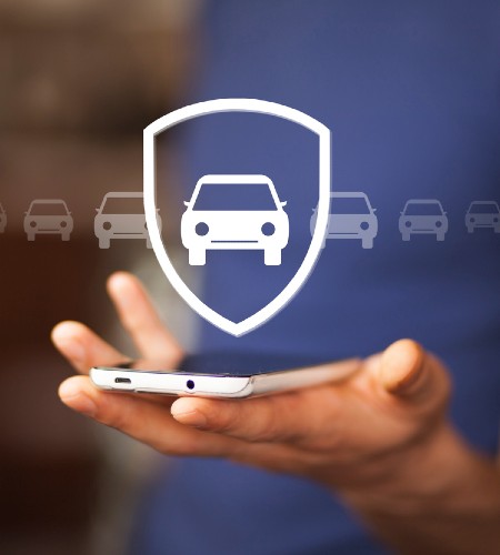 Άνδρας κρατά smartphone με εικονίδιο αυτοκινήτου και ασπίδας, συμβολίζοντας την ασφάλεια πυρός & κλοπής αυτοκινήτου.