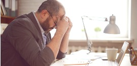 Απελπισμένος άνδρας κρατά το κεφάλι του πάνω από έγγραφα