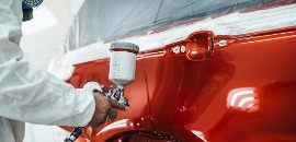 Μηχανικός με προστατευτικό εξοπλισμό βάφει αυτοκίνητο κόκκινο