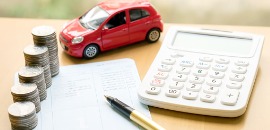 Τετράδιο περικυκλωμένο από στοίβες νομισμάτων, μοντέλο κόκκινου αυτοκινήτου, αριθμομηχανή και στυλό