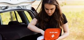 Γυναίκα οδηγός ελέγχει φαρμακείο αυτοκινήτου μπροστά από το ανοιχτό πορτ-παγκάζ του αυτοκινήτου της