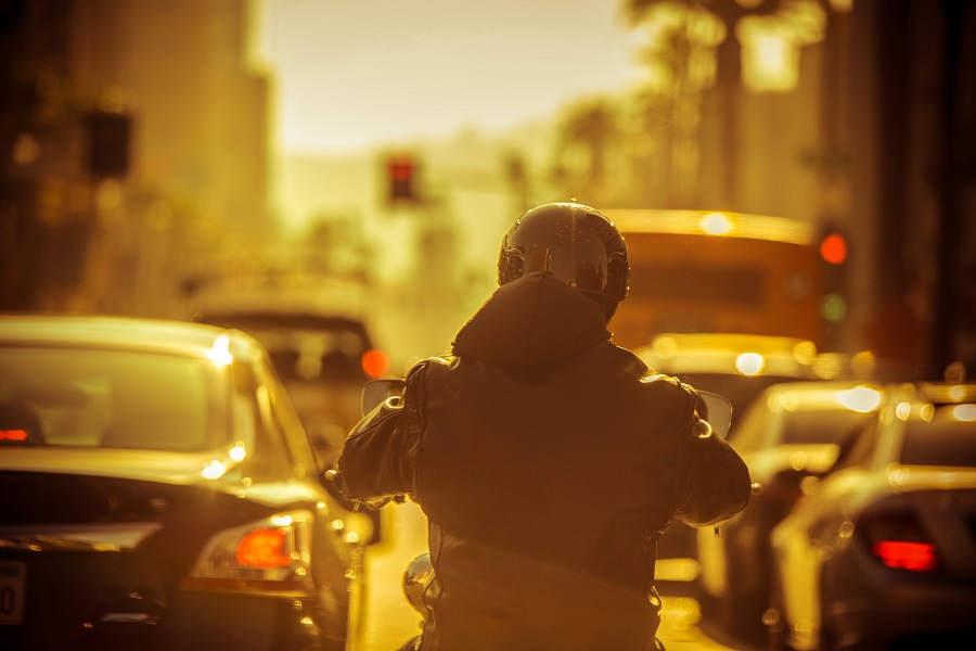 Οδηγός μηχανής περιμένει σε φανάρι πίσω από σειρά αυτοκινήτων υπό το φως του ηλιοβασιλέματος