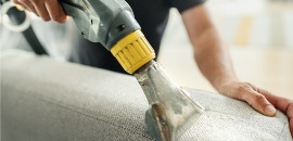 Χέρι κρατάει πλυστικό μηχανήμα και καθαρίζει ύφασμα καναπέ στο σπίτι για να ξεμυρίσει από καπνό
