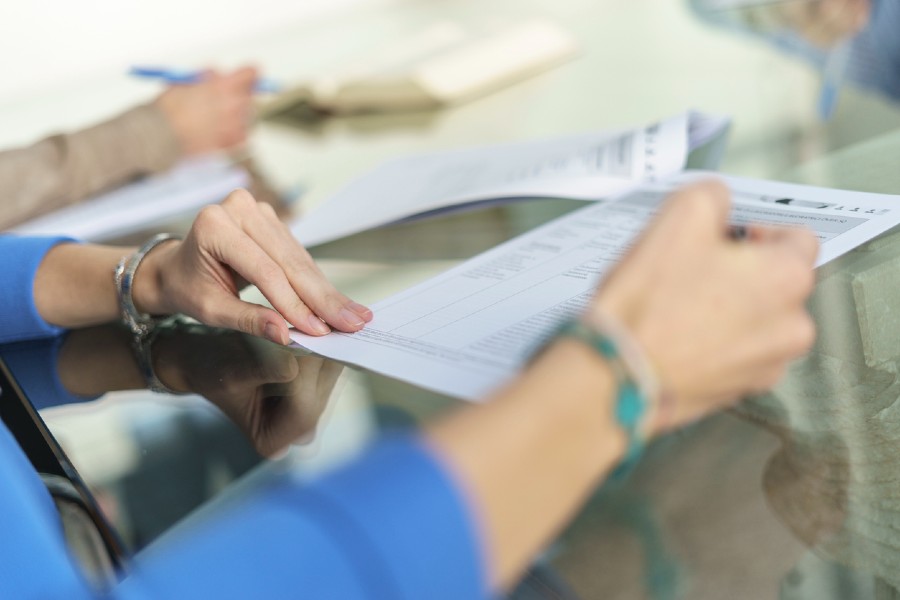 Γυνάικα συμπληρώνει έντυπο για Ταξινόμηση Οχήματος σε γραφείο, με έντυπα και στυλό πάνω σε γυάλινο τραπέζι.