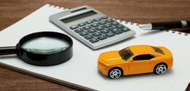 Τετράδιο πάνω στο οποίο υπάρχουν ένας μεγεθυντικός φακός, μια αριθμομηχανή, ένα στυλό και ένα μοντέλο πορτοκαλί αυτοκινήτου